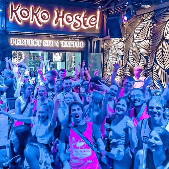 A group of people celebrating at Koko Hostel, with a neon sign and a tattoo shop visible. 2