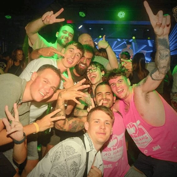 A group of people at a party, some making peace signs, with a DJ booth in the background. 4