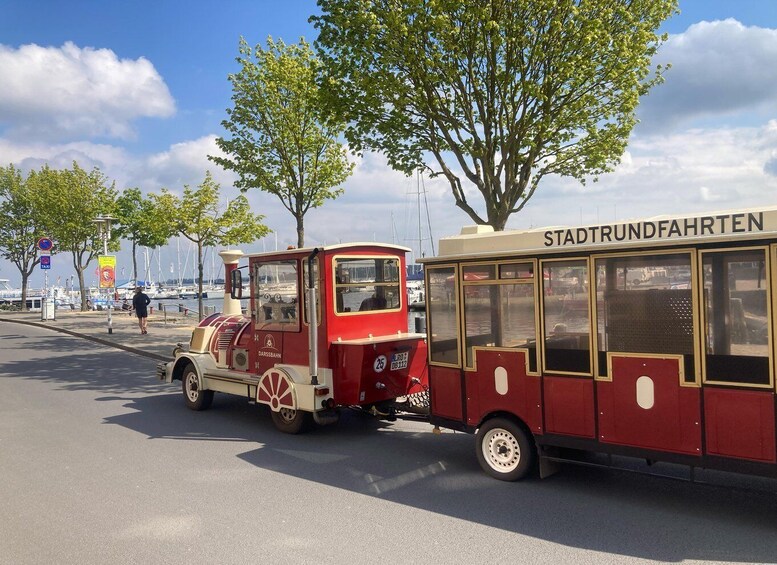 A vintage tram with 'STADTSTRUNDFAHREN' on the side, parked on a sunny street with trees and boats in the background. 3