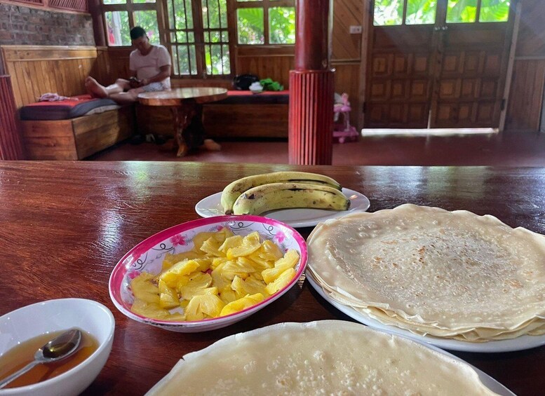 A wooden table with food items including bananas, pineapple, and a bowl of soup. 2