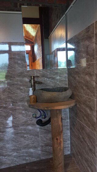 A bathroom with a stone sink, wooden base, and a mirror reflecting a wooden door and window. 3