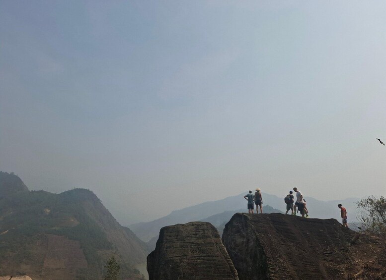 A group of hikers on a rocky outcrop with a valley and mountains in the background. 4