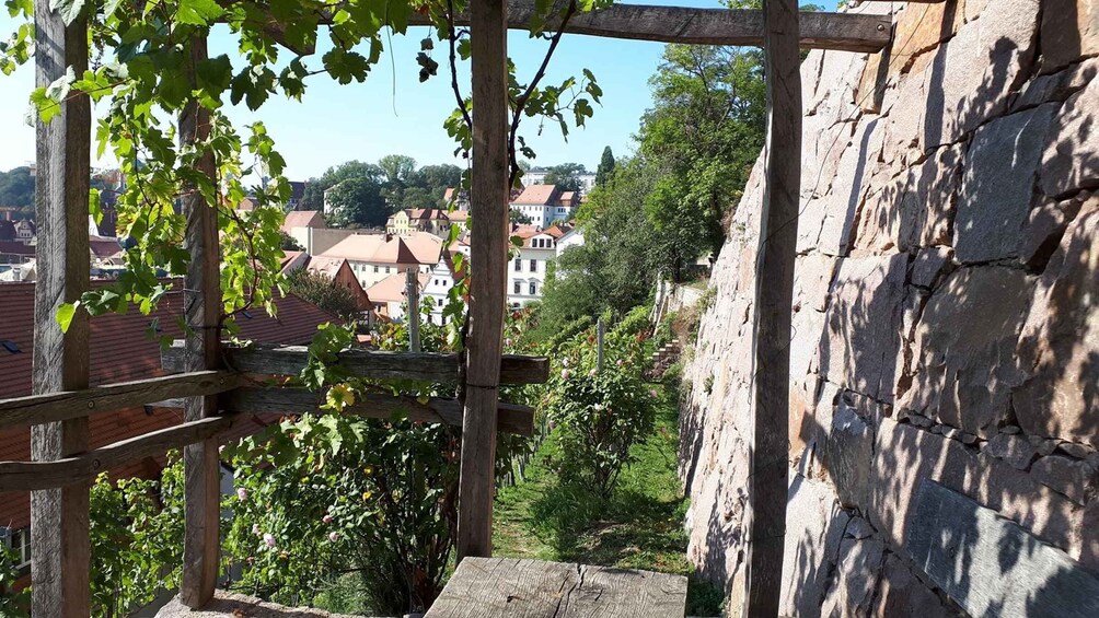 A stone wall with a wooden pergola overlooking a town with red-roofed buildings. 4