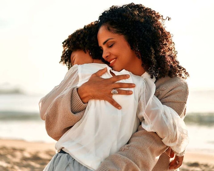 A person embracing another on a beach with sand and water in the background. 4