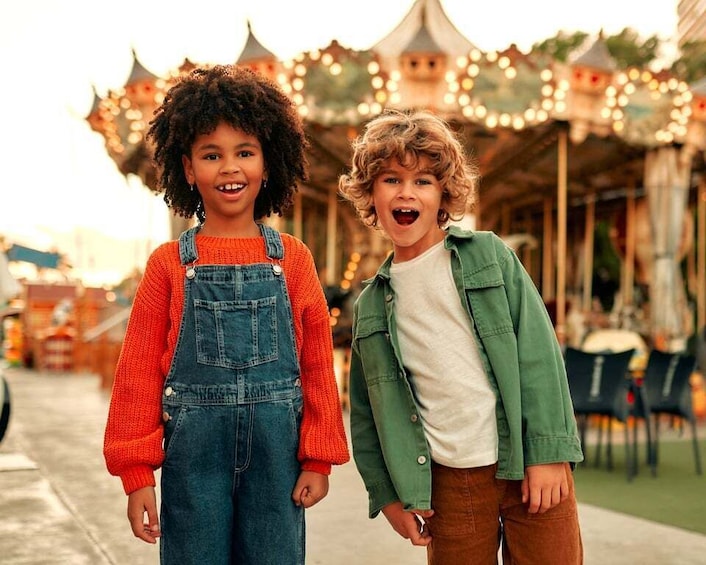 Two children standing in front of a carousel with lights. 5