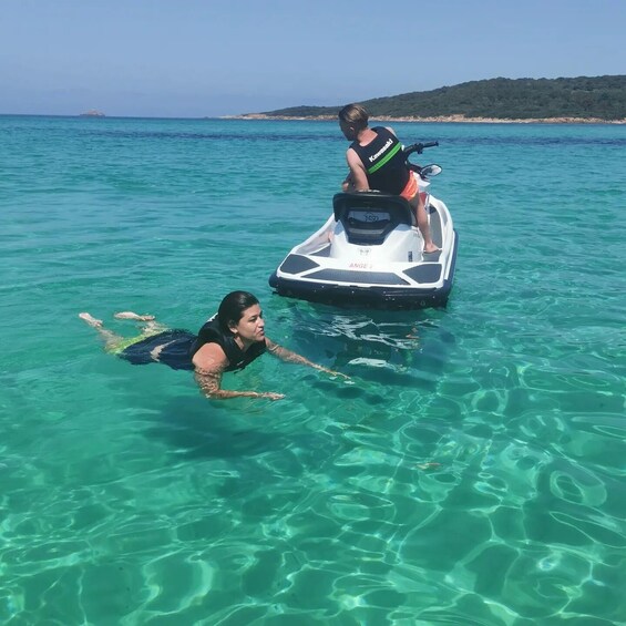 A person on a jet ski and another person swimming in clear turquoise water. 1