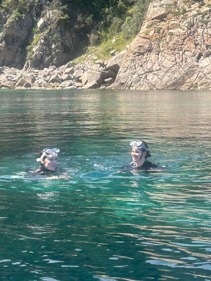 Two people swimming in clear water with rocky cliffs in the background. 3