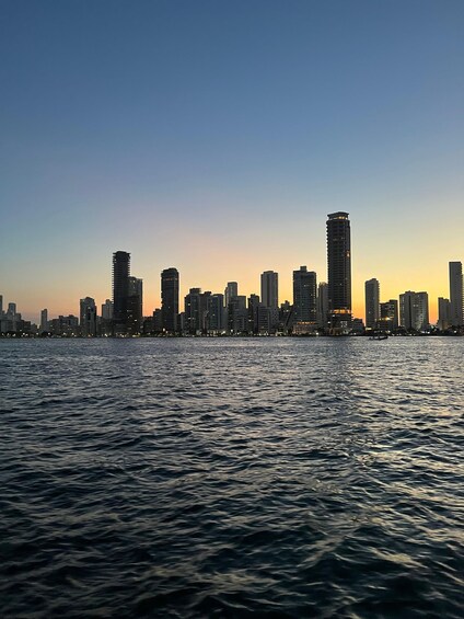 A city skyline at dusk with buildings silhouetted against a sunset sky, viewed from across a body of water. 5