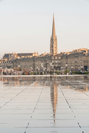 A cathedral with a tall spire, a wide reflective plaza, and historic buildings in the background. 4