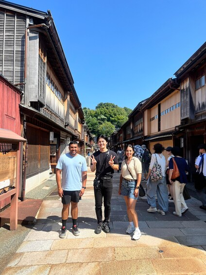 A narrow street lined with traditional wooden buildings, a clear blue sky, and a few pedestrians. 5