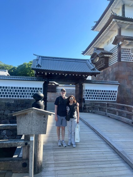A couple standing on a wooden bridge with traditional Japanese architecture in the background. 2