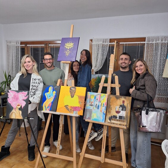 A group of people standing in a room with easels holding paintings. 1