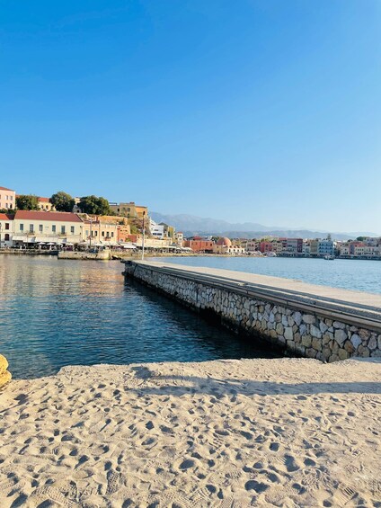 A coastal town with a stone pier extending into calm waters, sandy beach, and colorful buildings along the waterfront. 1