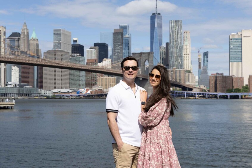 A couple standing in front of a city skyline with a river and a bridge. 1