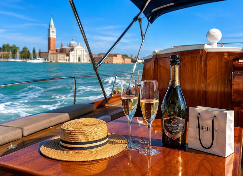 A boat with a bottle of Valdobbiadene Prosecco, two glasses of wine, a straw hat, and a Morellato shopping bag. 1