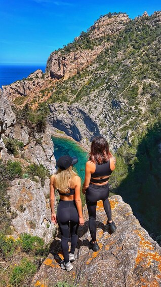 Two people standing on a rocky cliff overlooking a clear blue sea. 4