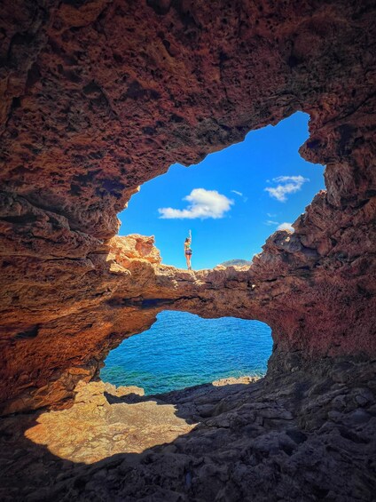 A person standing on a rock formation with a clear blue sky above and a body of water below. 5
