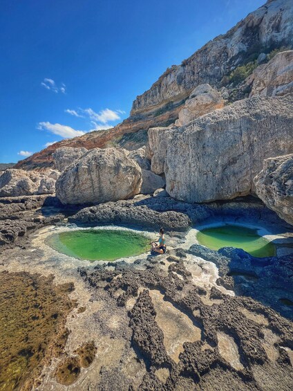 A person sitting on rocks by a green pool surrounded by large boulders. 3