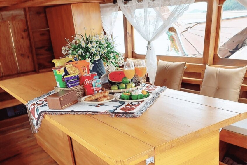 A wooden dining table with a placemat, food items, drinks, and a vase of flowers. 3