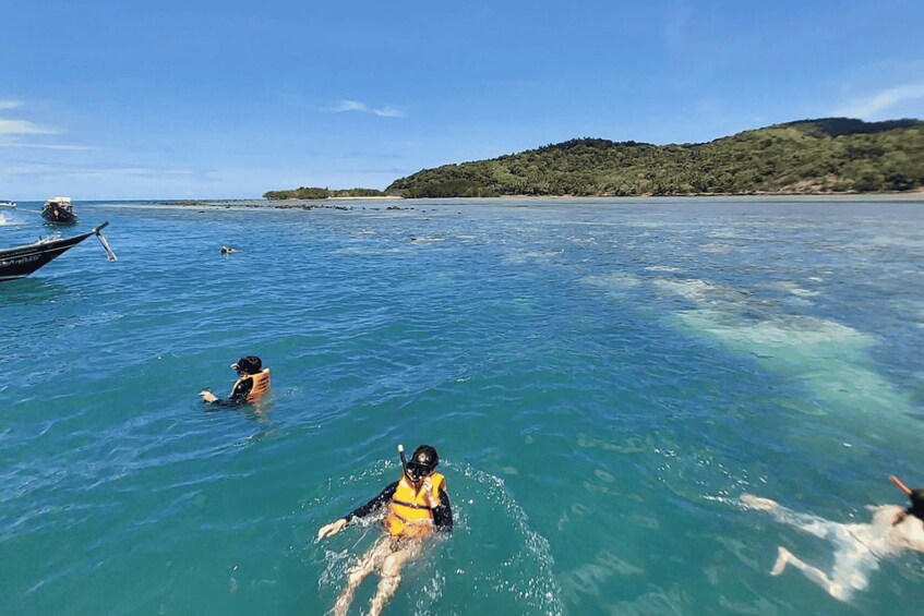 A person snorkeling in clear blue water with a boat and a beach in the background. 4