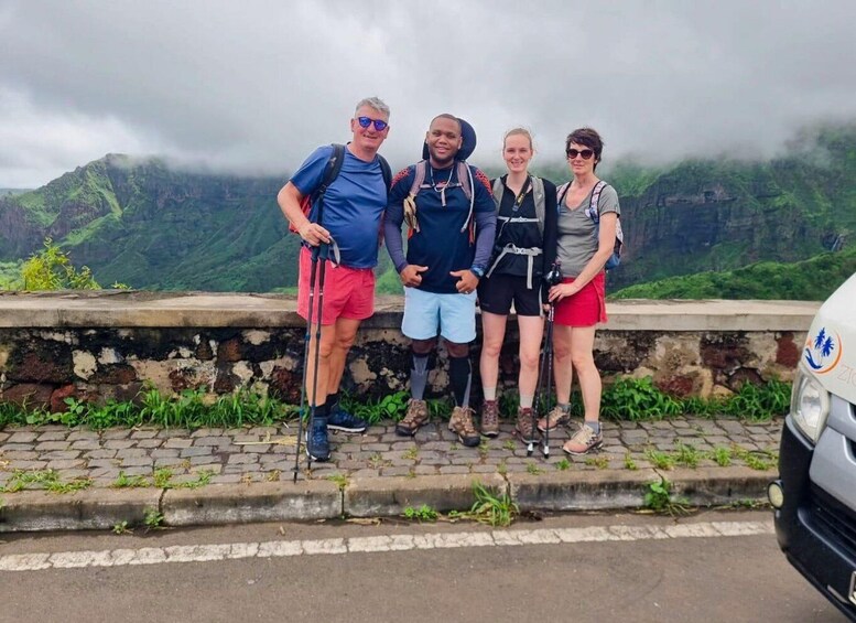 Four people standing on a stone wall with a mountainous landscape in the background. 5