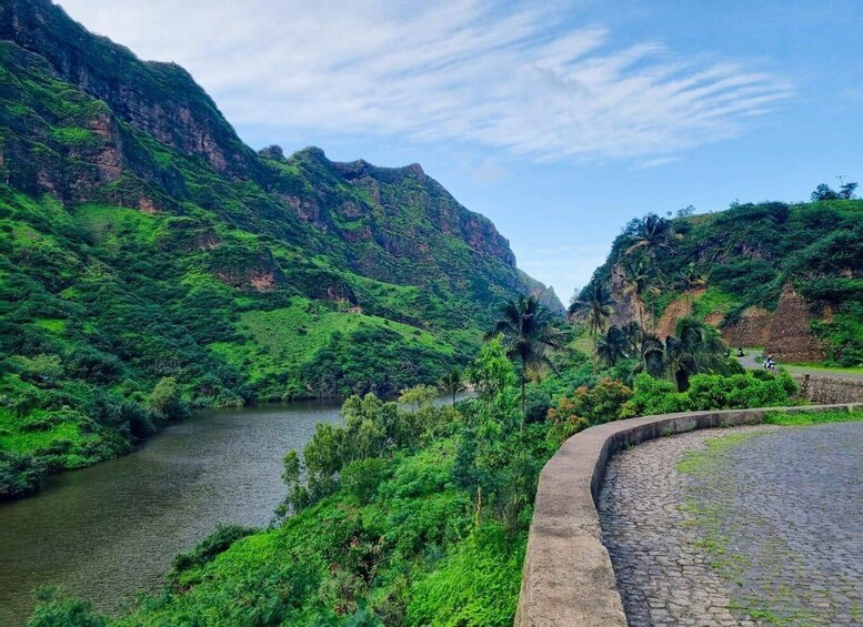A river winding through lush green hills with a stone bridge. 1