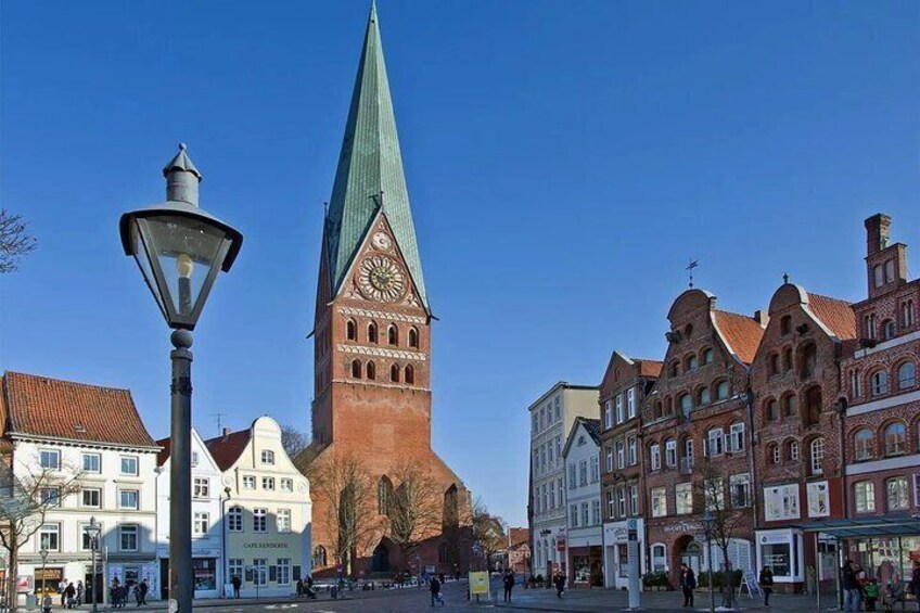 A historic tower with a clock, surrounded by traditional buildings and a clear blue sky. 1