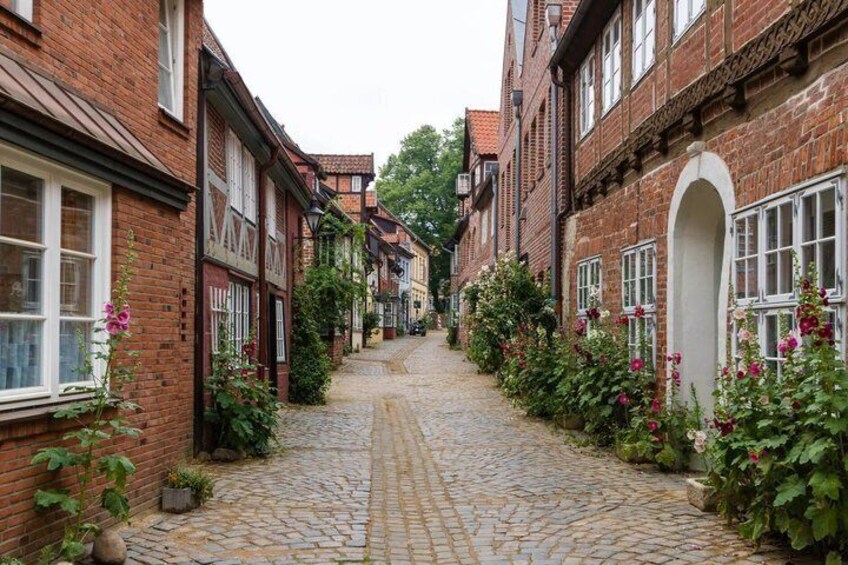 A cobblestone street lined with brick buildings, some with flower boxes and greenery. 2