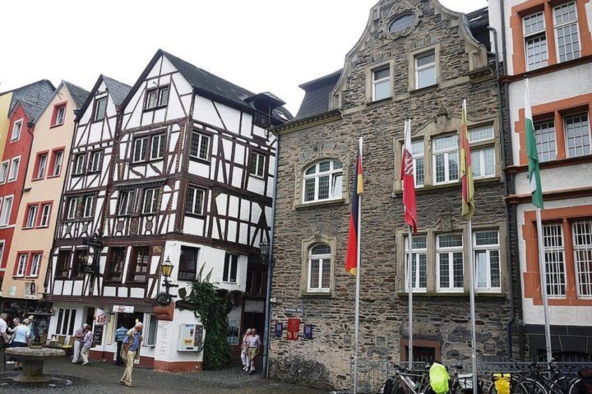 A historic European town with half-timbered buildings, flags, and a fountain. 4