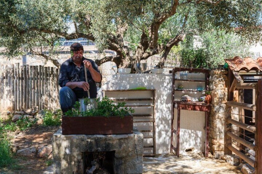 A man gardening in a rustic outdoor setting with a wooden bench, a stone planter, and a metal gate. 3