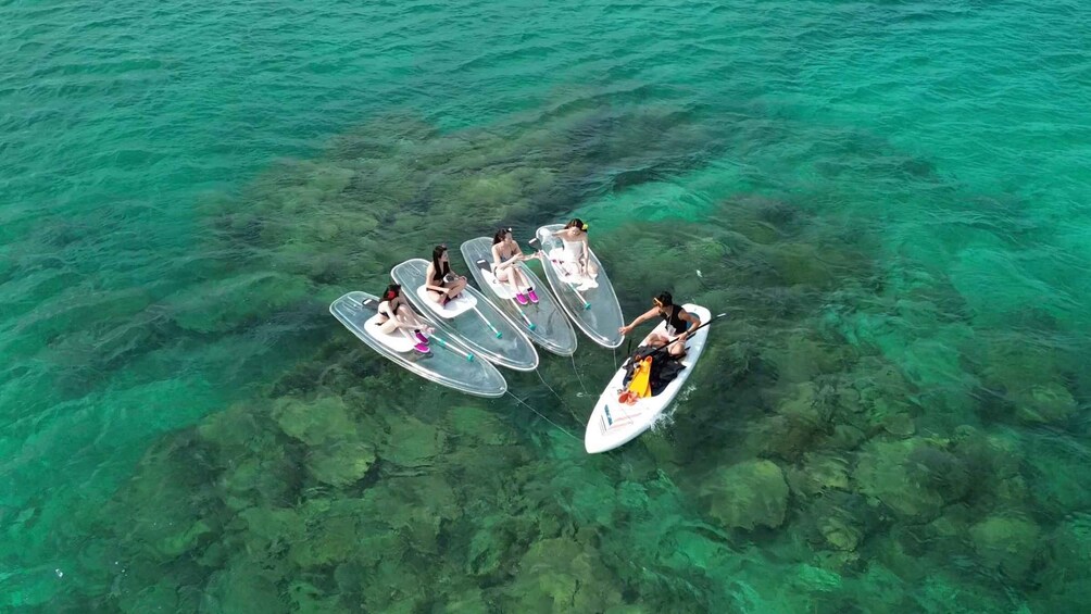 A group of people on clear waterboards and a small boat. 5