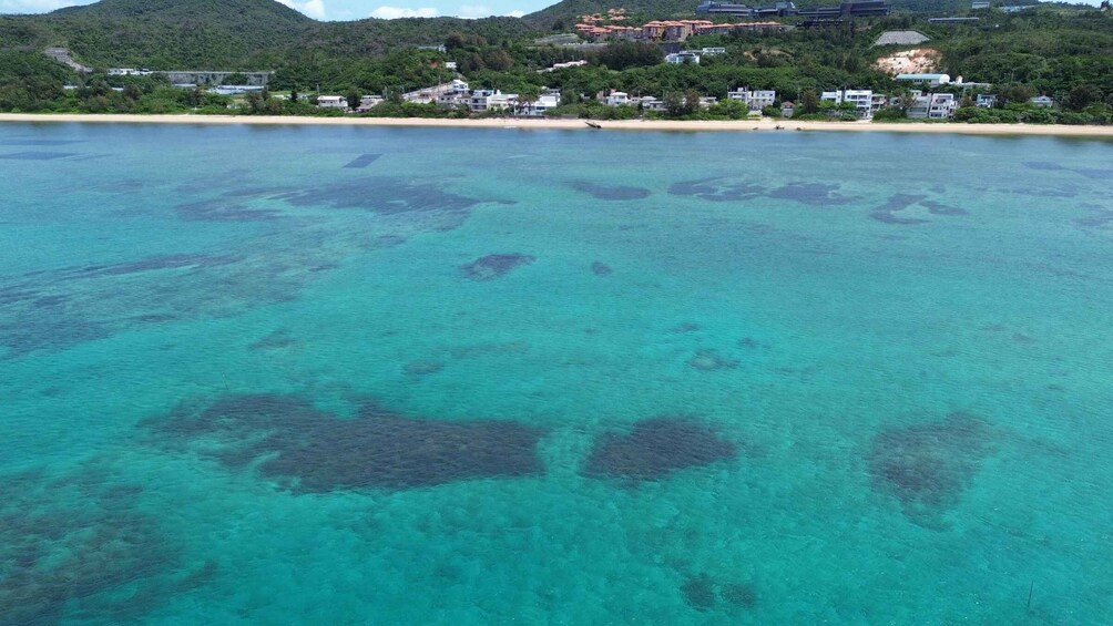 A coastal area with clear turquoise waters, a sandy beach, and a backdrop of residential buildings on a hillside. 3