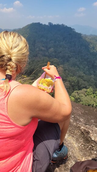 A person sitting on a rock, eating from a container with a spoon. 4
