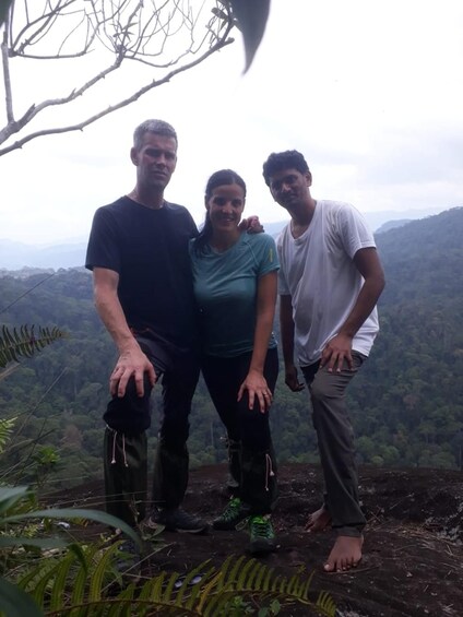 Three people standing on a mountain edge with a forested valley in the background. 2