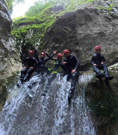 A group of people in wetsuits sitting on a rock by a waterfall. 5