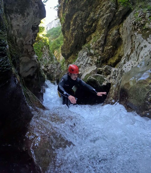 A person in a wetsuit and helmet navigating a narrow, rocky water passage. 2