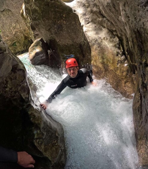 A person in a wetsuit and helmet navigating a narrow, rocky water passage. 4