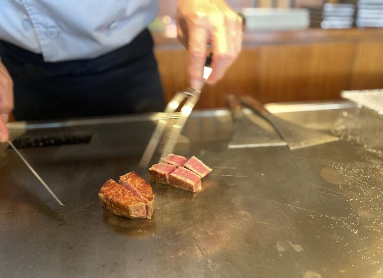 En person lagar mat på en het stekhäll, och skär upp kött i bitar. 2