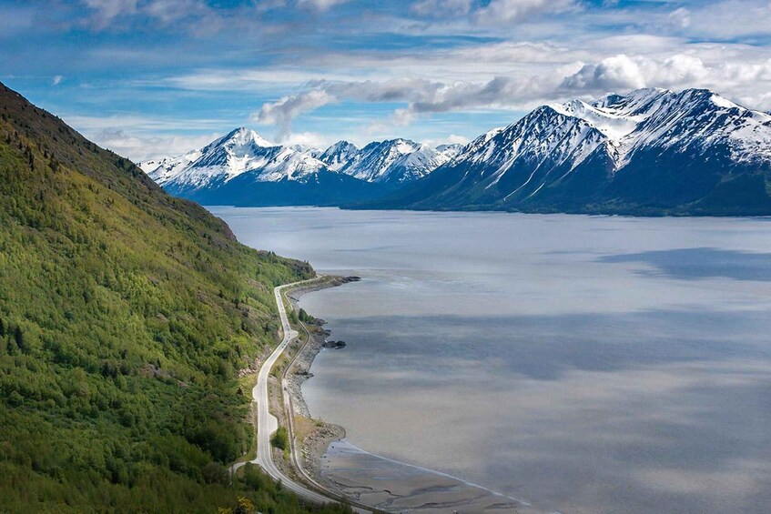 A mountainous landscape with a winding road, a large body of water, and snow-capped peaks. 1
