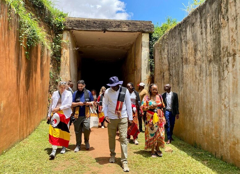 A group of people walking through a narrow passageway with a concrete wall on one side and a metal gate on the other. 3