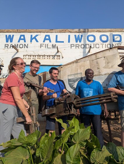 A group of people with a camera rig in front of a building with 'WAKALIWOOD' signage. 1