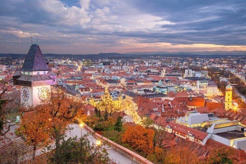 A cityscape with a prominent clock tower, autumn-colored trees, and a river. 3