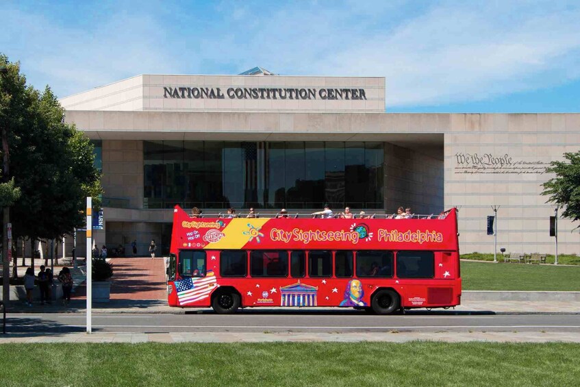 A red double-decker bus with 'City Sightseeing Philadelphia' branding parked in front of the National Constitution Center. 5
