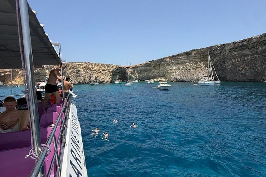 A boat with people swimming in the water, a rocky coastline, and sailboats in the distance. 5