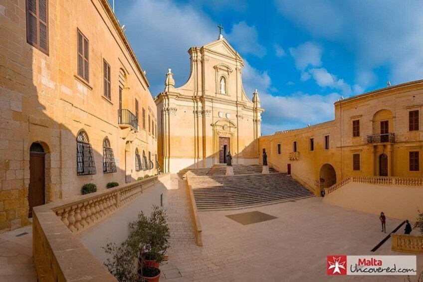 A historic building with a central staircase leading to a bell tower, surrounded by stone walls and potted plants. 3