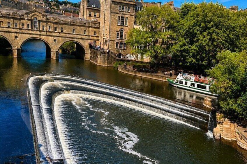 A river with a water cascade, a boat, and a historic building with arches. 3
