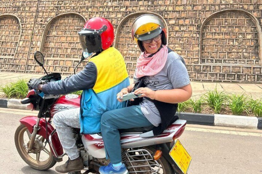 Two people on a motorcycle with a brick wall in the background. 2