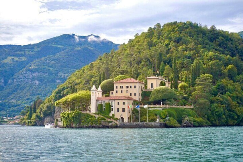 A lakeside villa with a tower, surrounded by lush greenery and mountains. 1