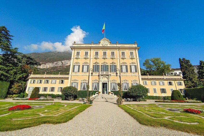A large, yellow building with a flag, surrounded by well-manicured gardens and a mountain in the background. 4