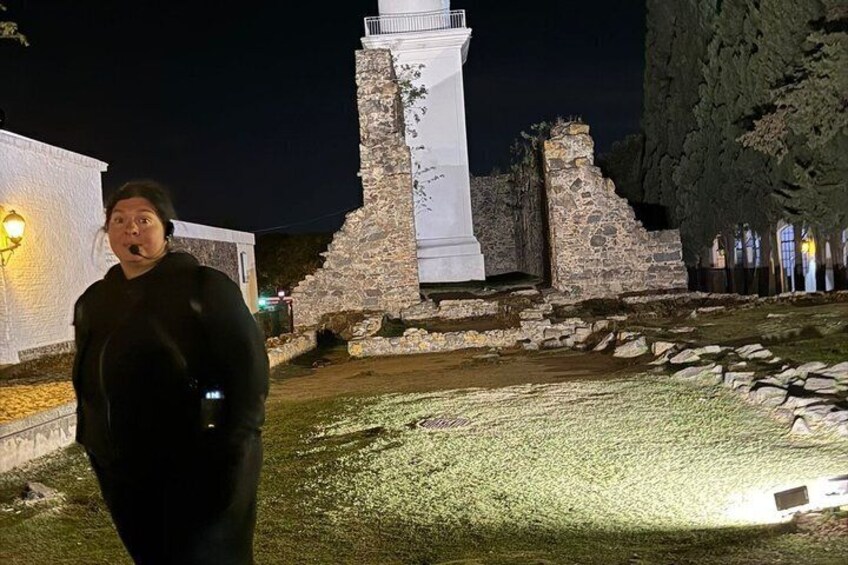 A person standing in front of a stone structure with a white tower, possibly a lighthouse, at night. 4